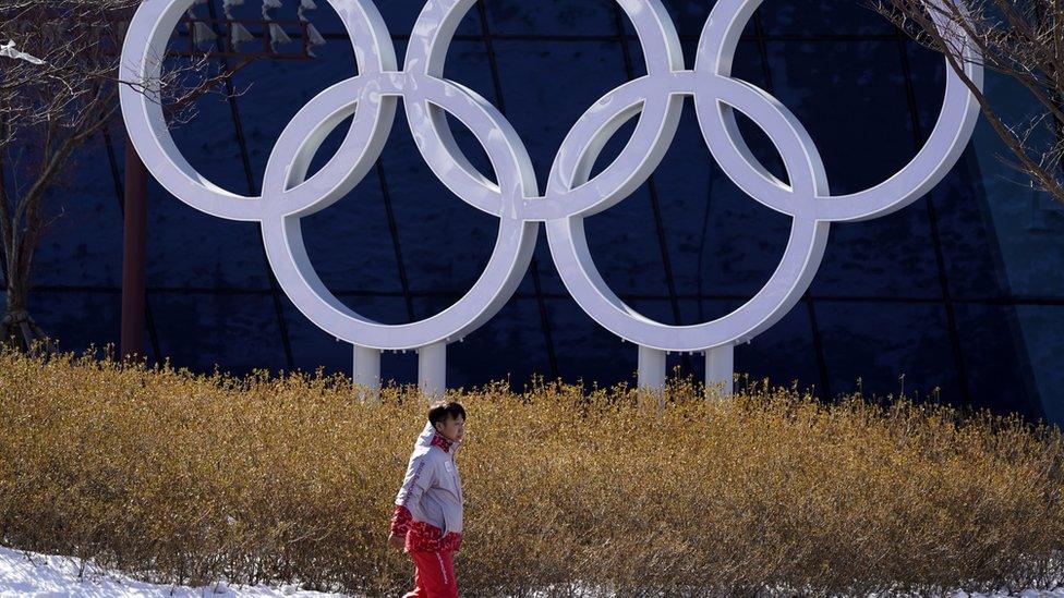 A volunteer walks past the Olympics Rings installation at the Olympic Village