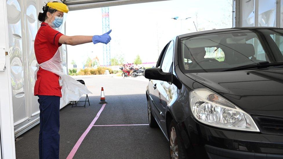 A member of clinical staff wears Personal Protective Equipment (PPE) as she gestures to a key worker at a drive-through test centre for the novel coronavirus at Royal Papworth Hospital in Cambridge on May 5, 2020. - NHS services have come under increased strain with the number of a patients hospitalised and requiring critical care because of the COVID-19 pandemic which has claimed over 30,000 lives in the UK. Mass testing has become a key part of the UK strategy in their battle against the virus.