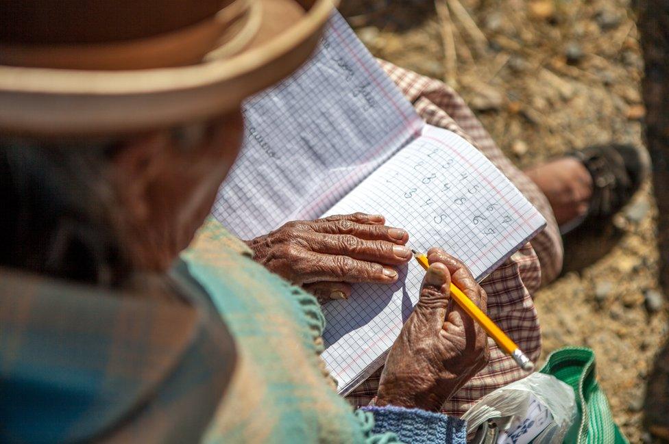 An elderly student writes down numbers from one to seven in a notebook