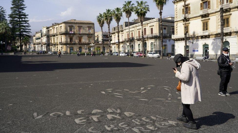 A person stands next to a sign made with ashes from Mount Etna that reads "Etna volcano what a nice gift" in Giarre, Italy, February 28, 2021