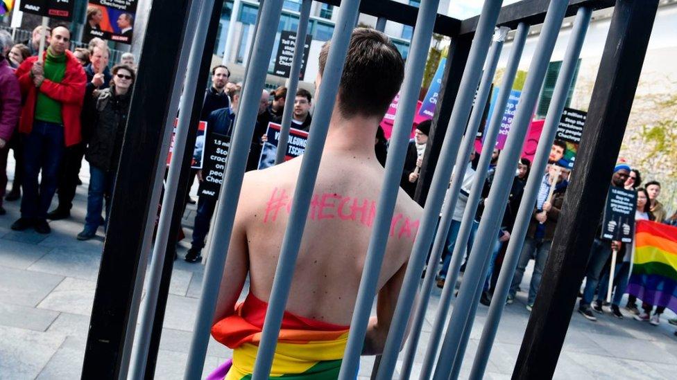 An activist stands naked, wrapped in a rainbow flag, in a mock cage in front of the Chancellery in Berlin on April 30, 2017, during a demonstration calling on Russian President to put an end to the persecution of gay men in Chechnya