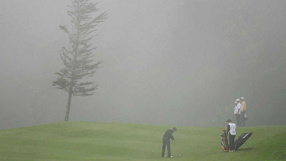 Golfers play in foggy conditions.