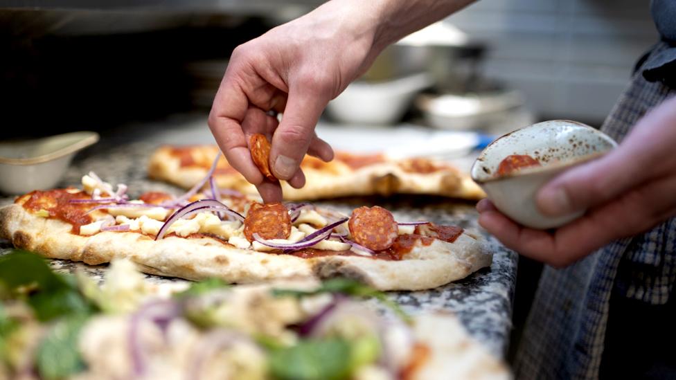 Stock image of someone putting toppings on a pizza