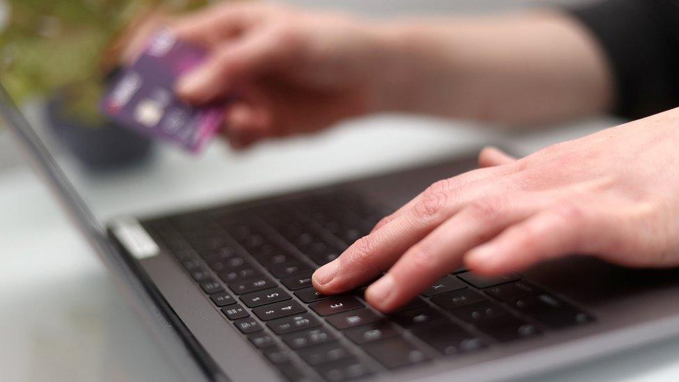 Person typing on keyboard while holding debit card