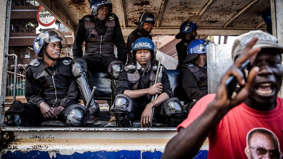 Zimbabwean anti riot police officers observe a supporter of the opposition party Movement for Democratic Change (MDC) who is taking part in a protest against alleged widespread fraud by the election authority and ruling party, after the announcement of the election's results, outside the Zimbabwe Electoral Commission (ZEC) headquarters in Harare, 1 August 2018