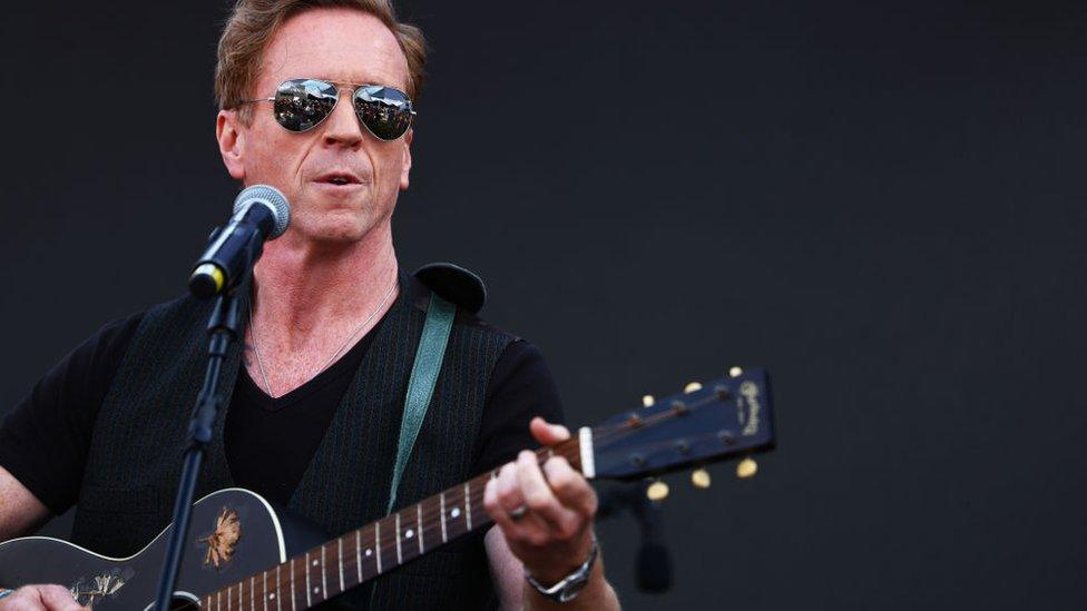 Damian Lewis performing with a guitar