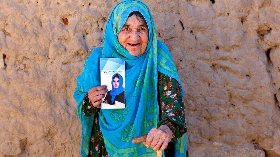 A woman in a camp for internally displaced people in Kabul holds an election pamphlet