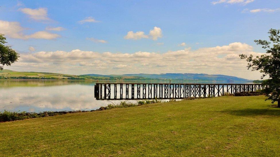 A pier in the distance with the River Clyde reflecting the clouds and pier