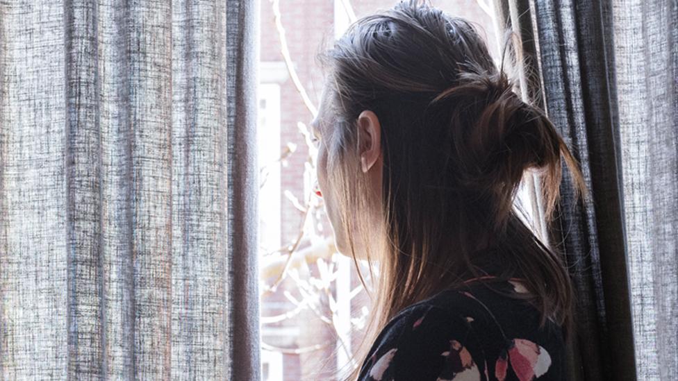 Stock image of an anonymous woman looking through bedroom curtains