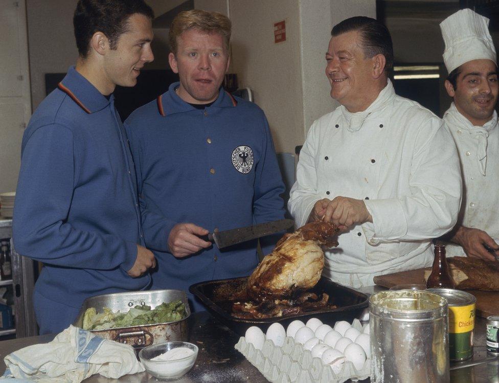 West German footballers Franz Beckenbauer and Helmut Haller helping the Peak Hotel cook prepare dinner while staying in Peveril, during the 1966 World Cup in England, 14 July 1966. (Photo by Central Press/Hulton Archive/Getty Images)