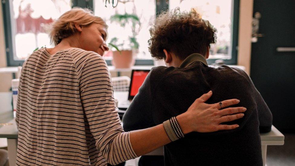 Parent has arm around child comforting them as they do school work