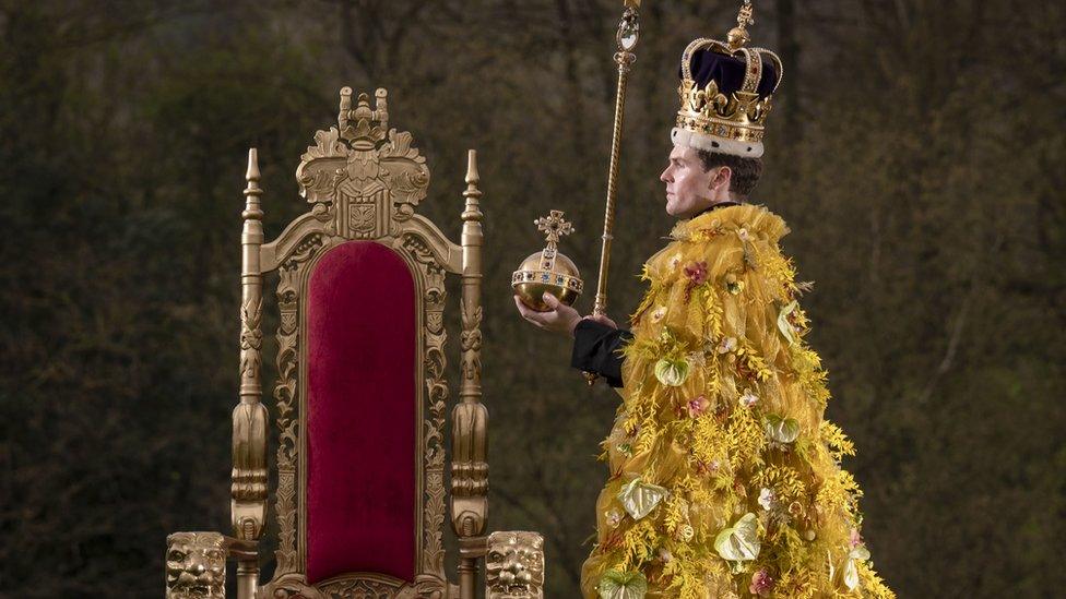 Model wearing robe made of flowers, a replica crown and holding a sceptre and orb