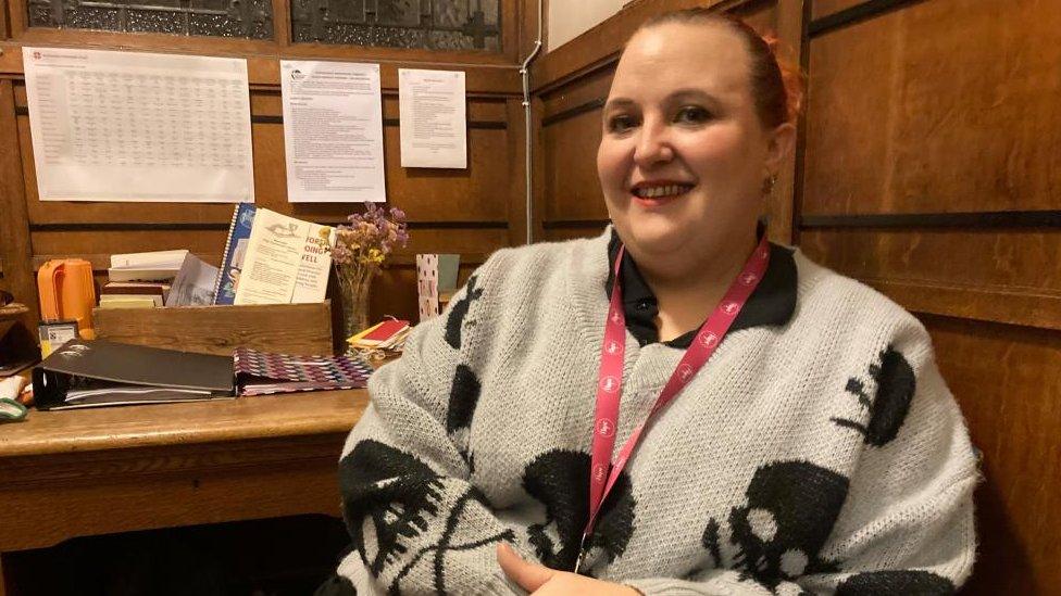 Woman wearing lanyard sits at a desk in an office with wooden walls