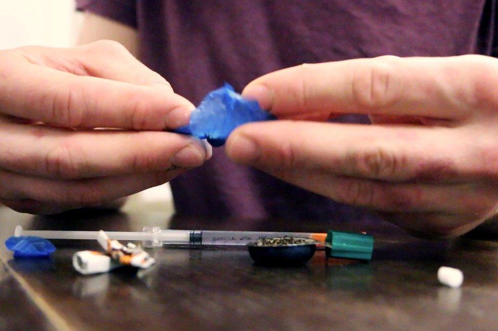 Elliot removing drugs from a blue bag