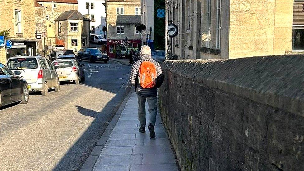 A person walking on the pavement on the bridge, with a queue of traffic on the other side