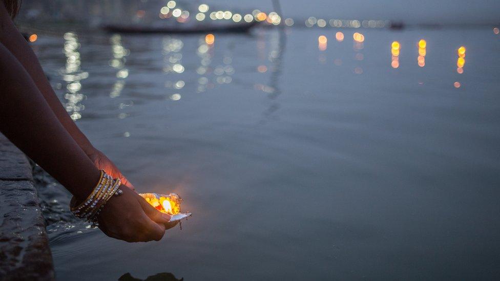 Woman putting blessed puja flowers in the river Ganges in Varanasi, India