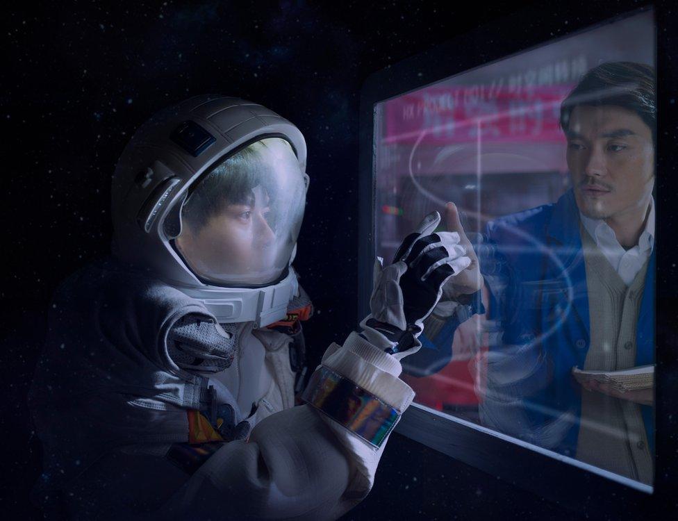 A photo by Cao Fei showing an astronaut touching a glass pane with a person on the other side