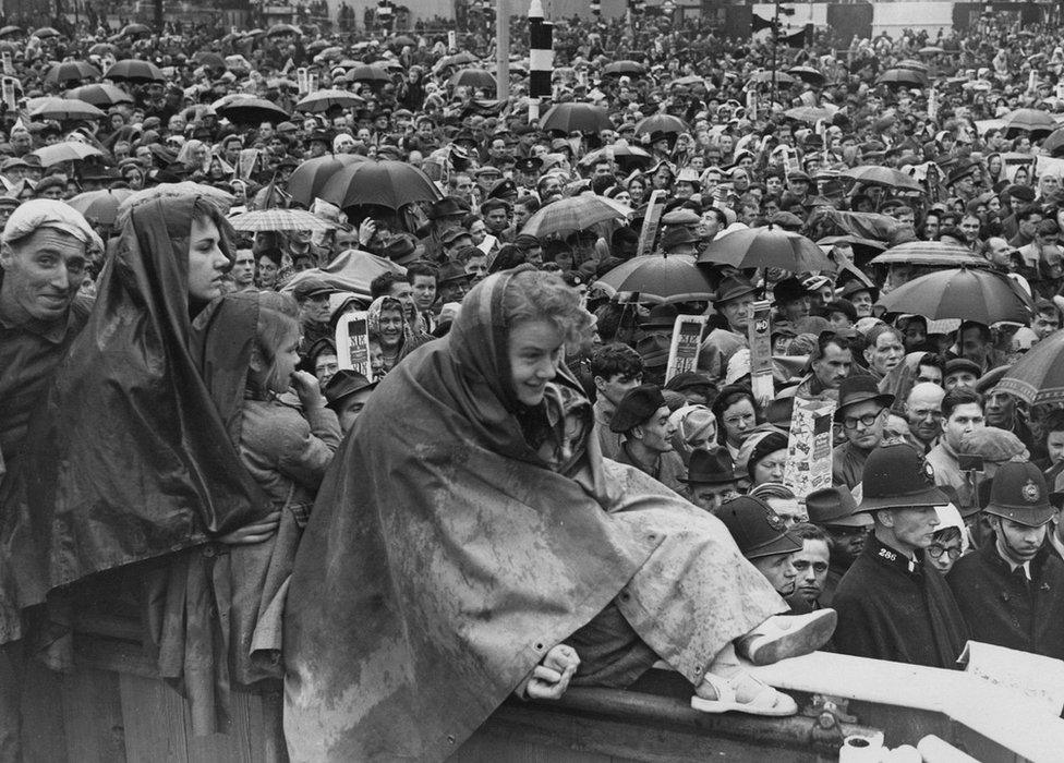 The crowds in Trafalgar Square, with umbrellas and hoods up against the rain, on the day of the Queen's Coronation 1953