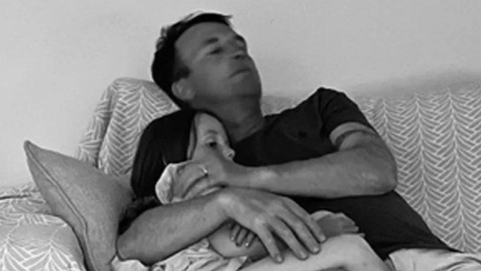 Hollie's husband Mike cuddling Sydney on the sofa. The photo has a black and white treatment.