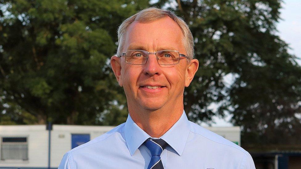 Neil Blackmore looks into the camera, wearing glasses and a blue shirt & tie