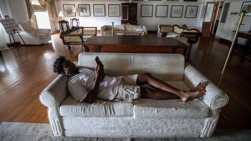 A man lies on a sofa looking at his phone in the Sri Lankan president's official residence on Sunday