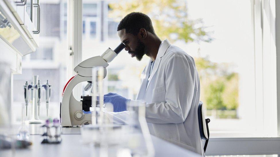 Man in lab coat, looking into microscope