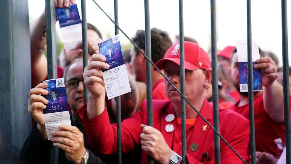 Liverpool fans stuck outside the stadium show their match tickets