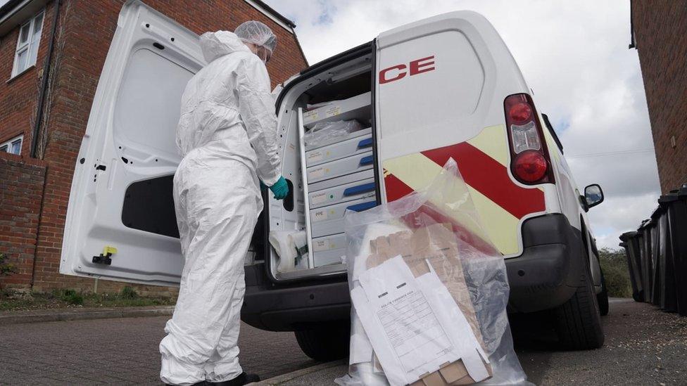 A forensic officer standing at the back of a police van