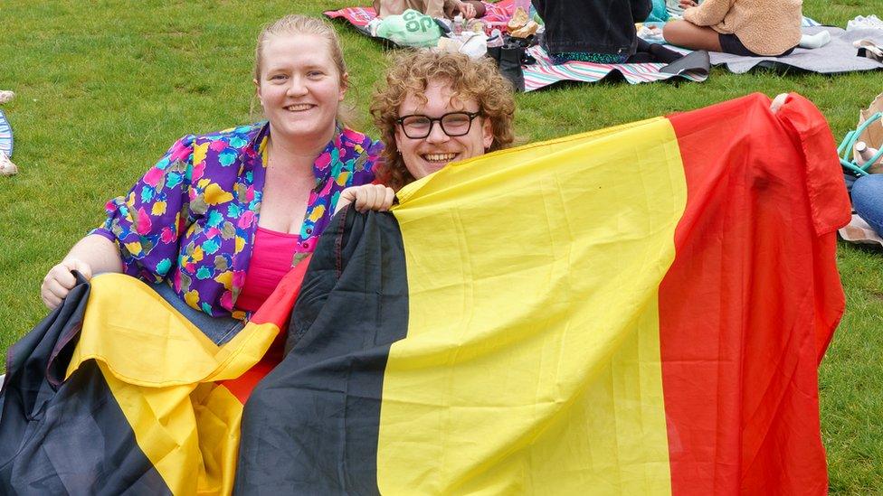 Two Germany fans show off their flags while seated in the park.