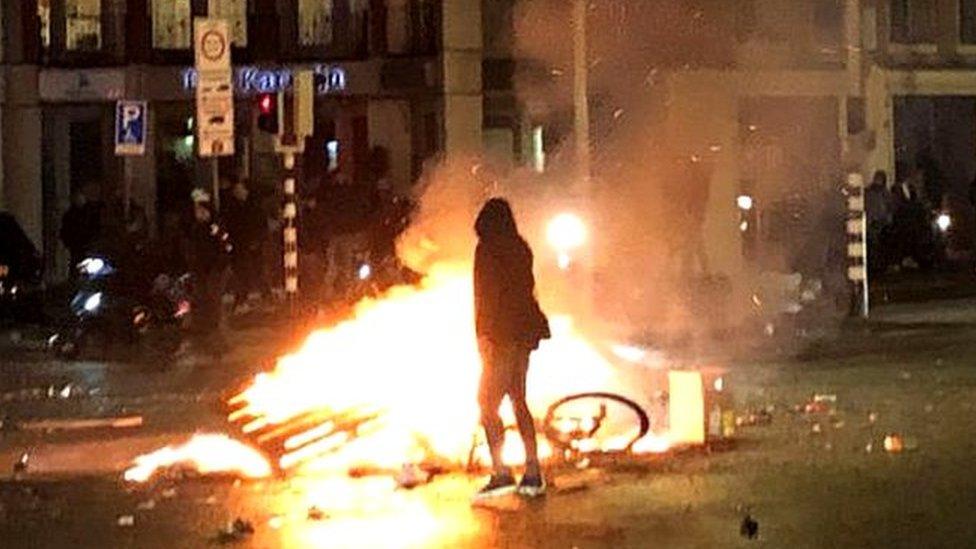 silhouette of person standing by bike on fire at Dutch protest