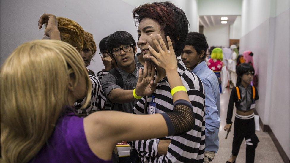 Young men and women apply makeup to a young mans face