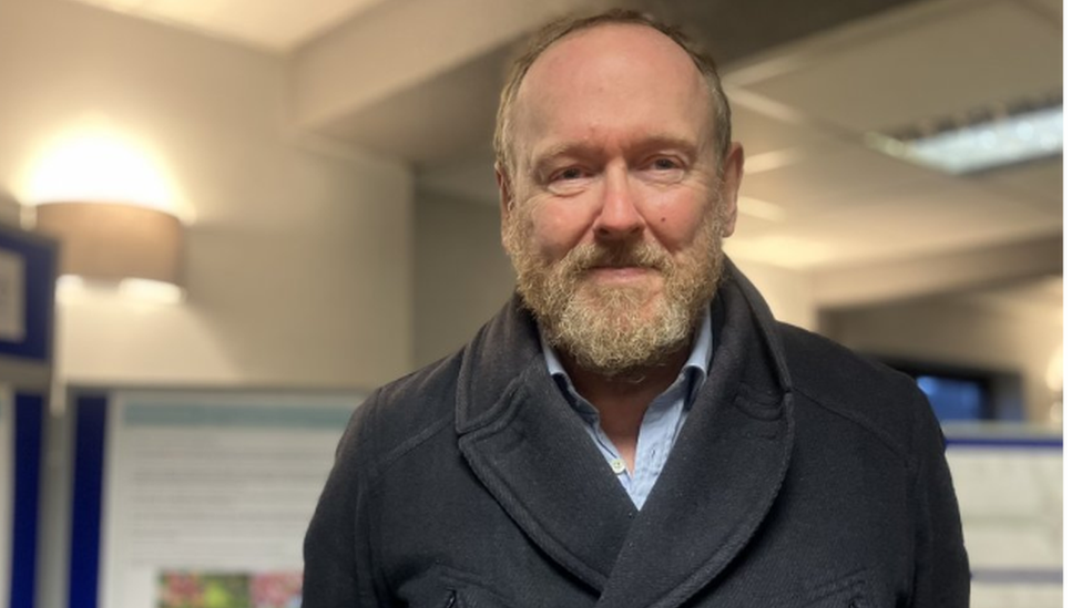 A man in a coat with a beard staring ahead at the camera