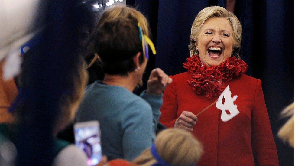 Hillary Clinton laughs as she holds a face mask