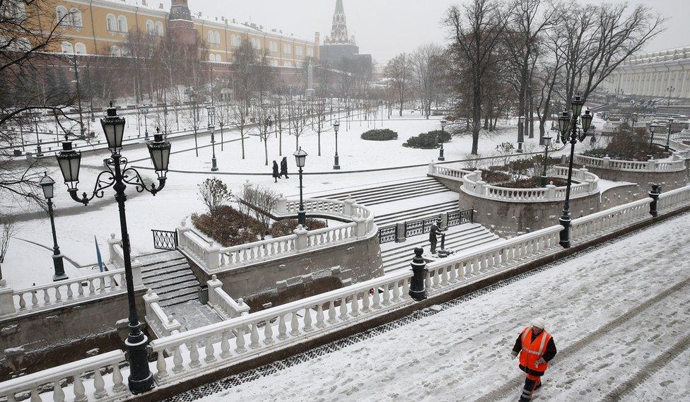 A worker walks near the Kremlin after a snowfall in central Moscow (30 Nov)