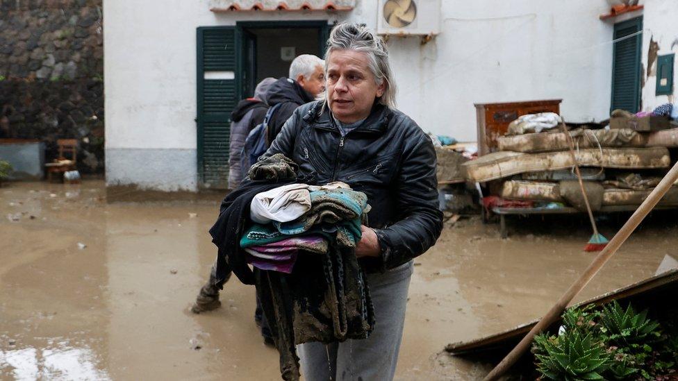 A resident carries some belongings covered in mud