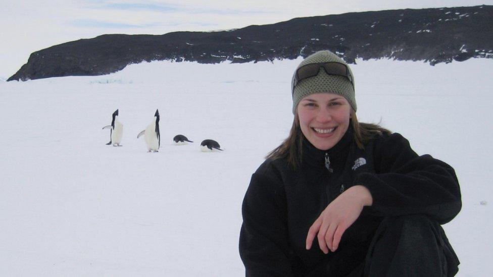 A woman kneels in the snow in front of some penguins