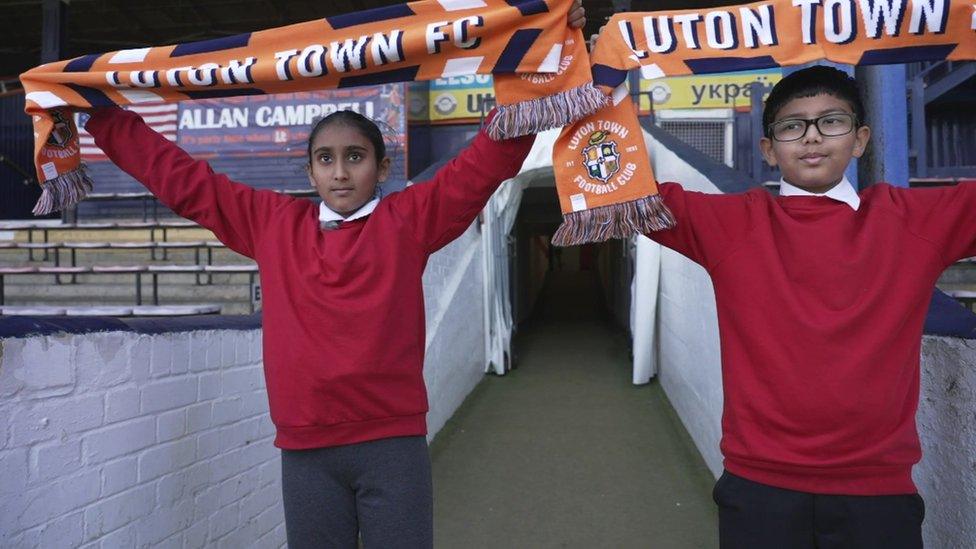 Kids hold up Luton FC scarves.