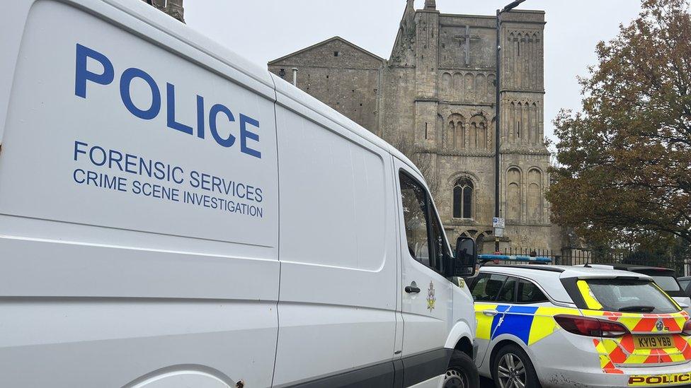 The side of a police forensics van, part of a police car and the abbey in the background.