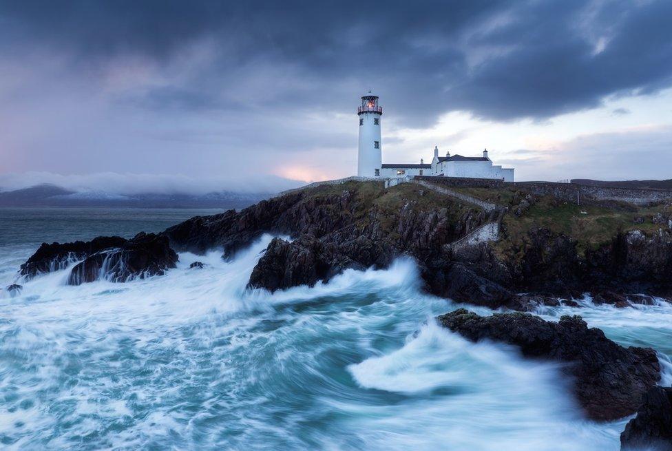 Storm clouds over Fanad lighthouse in County Donegal as waves crash against the rocks