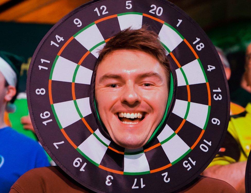 A man smiling at the camera wears a replica round foam dartboard