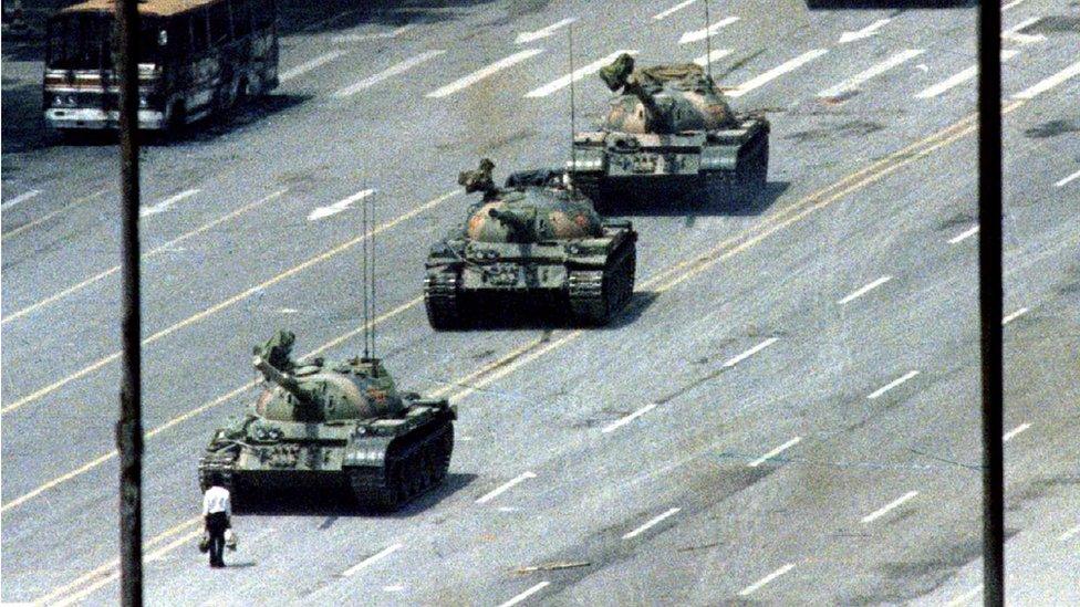 A man stands in front of three tanks