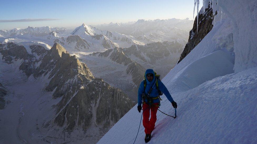 A man climbing through an ice gorge with the Himalayas in the background