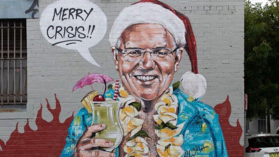 A wall mural depicting Scott Morrison, dressed in a Hawaiian shirt and Santa hat while holding a cocktail against a backdrop of flames, saying "Merry Crisis".