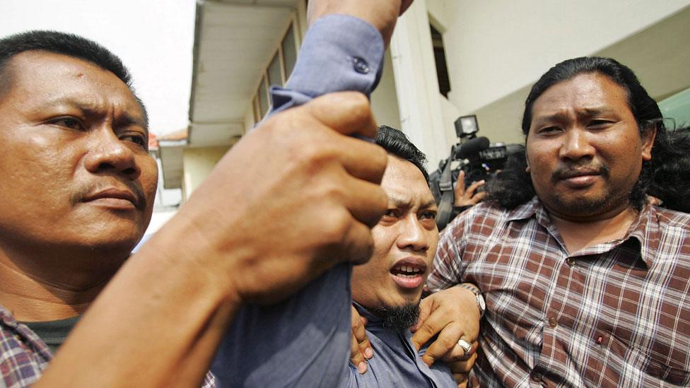 Hassan raising his fist in defiance as he leaves court