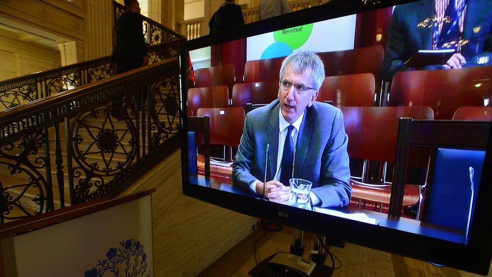 A TV screen in Parliament Buildings shows Máirtín Ó Muilleoir appearing before Stormont's Finance Committee