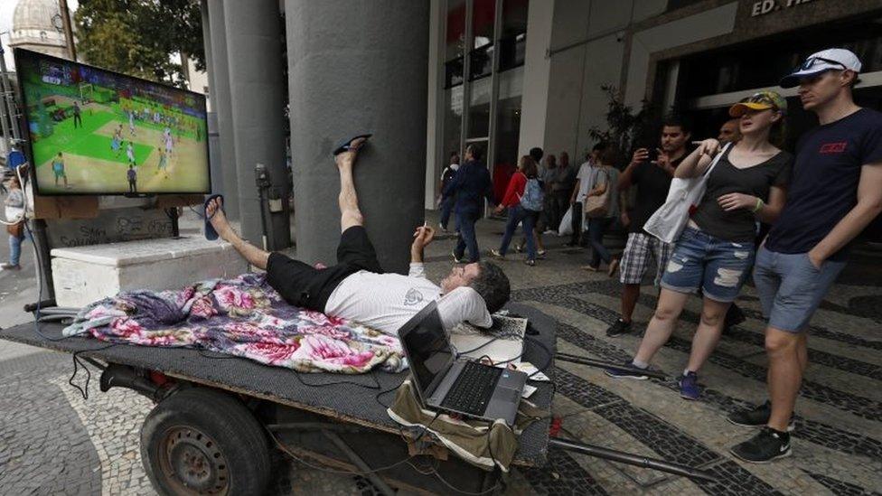 Tourists join the viewing with a Brazilian man as he uses his street cart rigged with a TV showing Olympic competition to watch the Olympic basketball match between Serbia and Australia at a traffic light in Centro district, during the Rio 2016 Olympic Games in Rio de Janeiro, Brazil, 08 August 2016