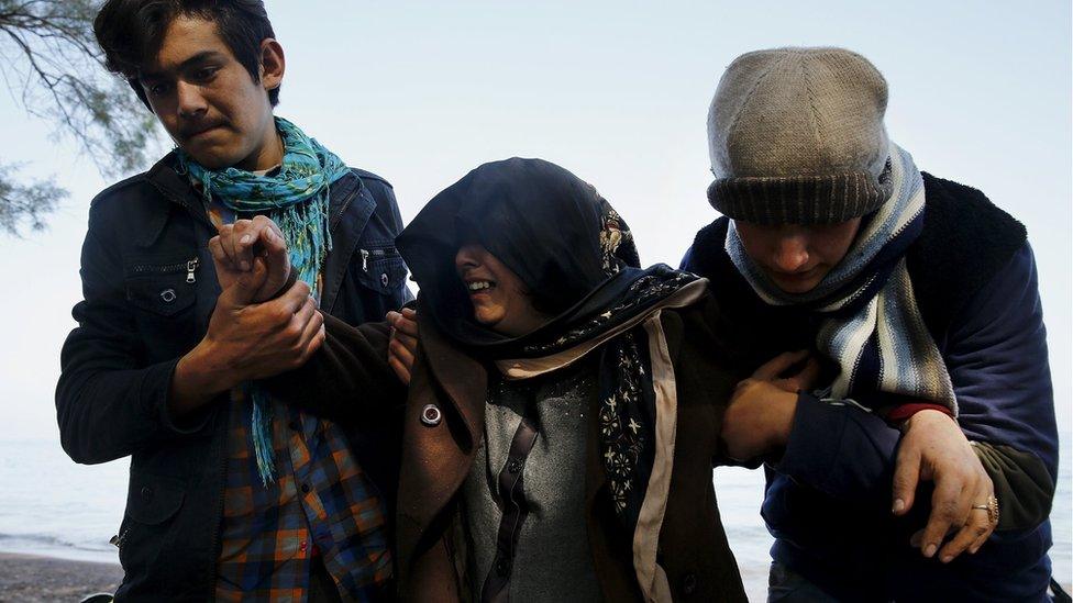 An Afghan migrant woman cries as two relatives help her walk soon after arriving on an overcrowded raft at a beach on the Greek island of Lesbos