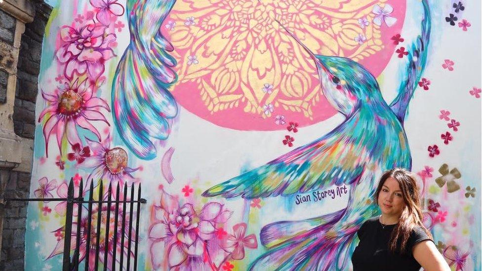 Sian Storey with an art mural of two humming birds