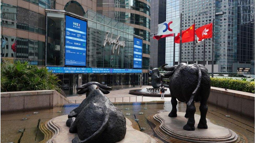 Flags flutter next to the Hong Kong stock exchange, surrounded by glass-fronted skyscrapers.