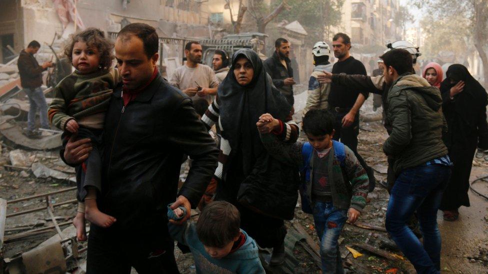 Syrians make their way through debris (rubble, wreckage) as they leave for a safer place following air strikes in the rebel-controlled side of the northern city of Aleppo on January 13, 2016.